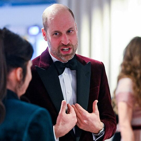 Britain's Prince William, Prince of Wales, meets with Jane Millichip, CEO of the British Academy of Film and Television Arts. He is pictured speaking to her while wearing a maroon velvet suit.
